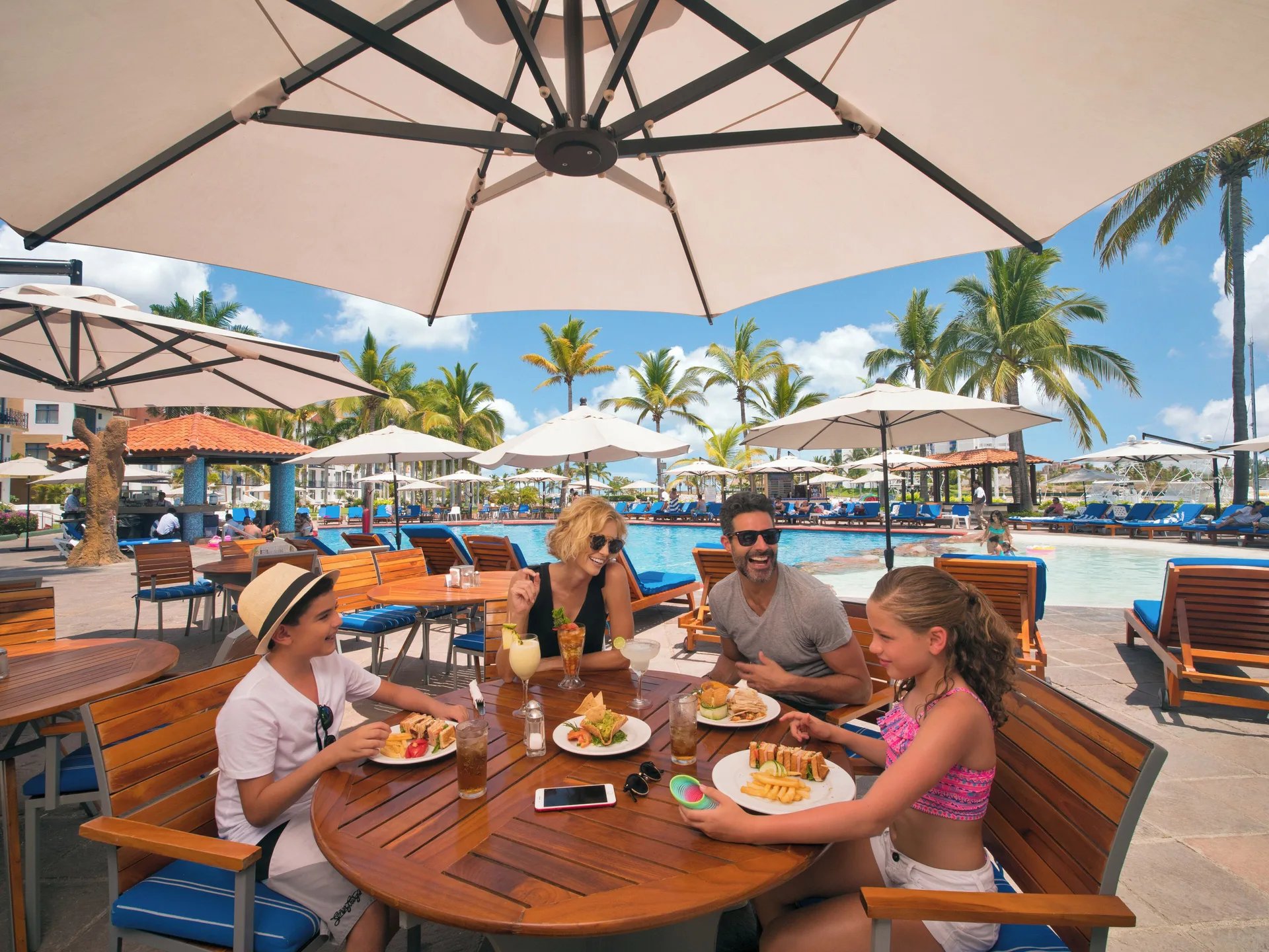 Poolside family dining under umbrellas at El Cid Marina Beach Hotel.