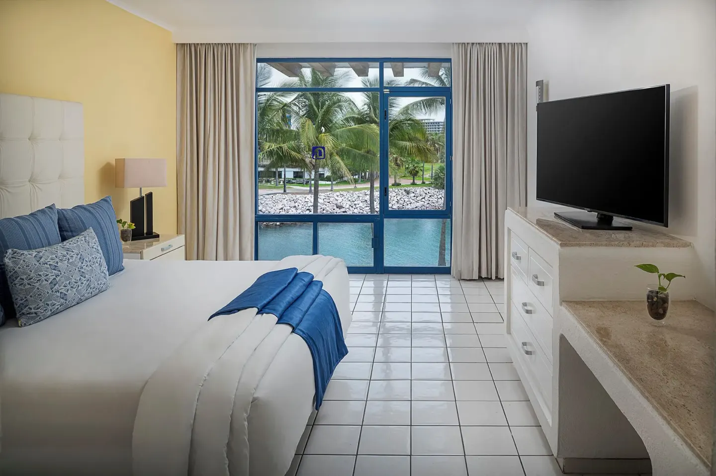 One Bedroom Suite king bed facing blue-framed windows at El Cid Marina Beach Hotel.