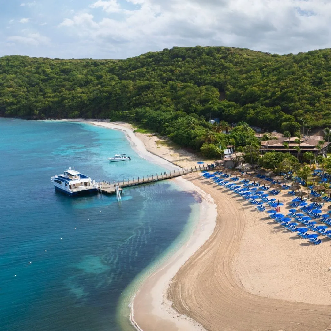 Beach with lounge chairs, dock, and clear water at El Conquistador Resort.