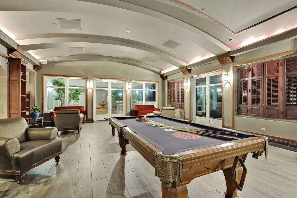 Indoor game room with pool table, lounge chairs, and shuttered windows at El Conquistador Resort.