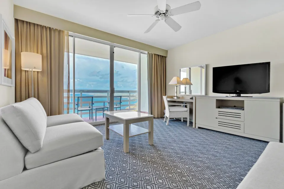 Living area with balcony ocean view, sofa, desk, and TV at El Conquistador Resort.