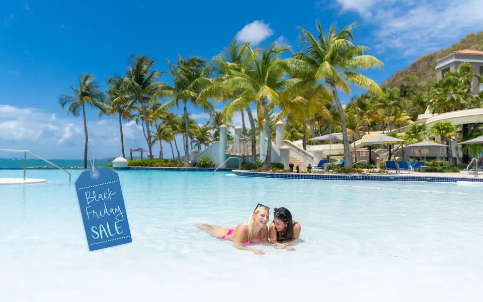 Guests relax in a palm-lined pool with a sale sign at El Conquistador Resort.