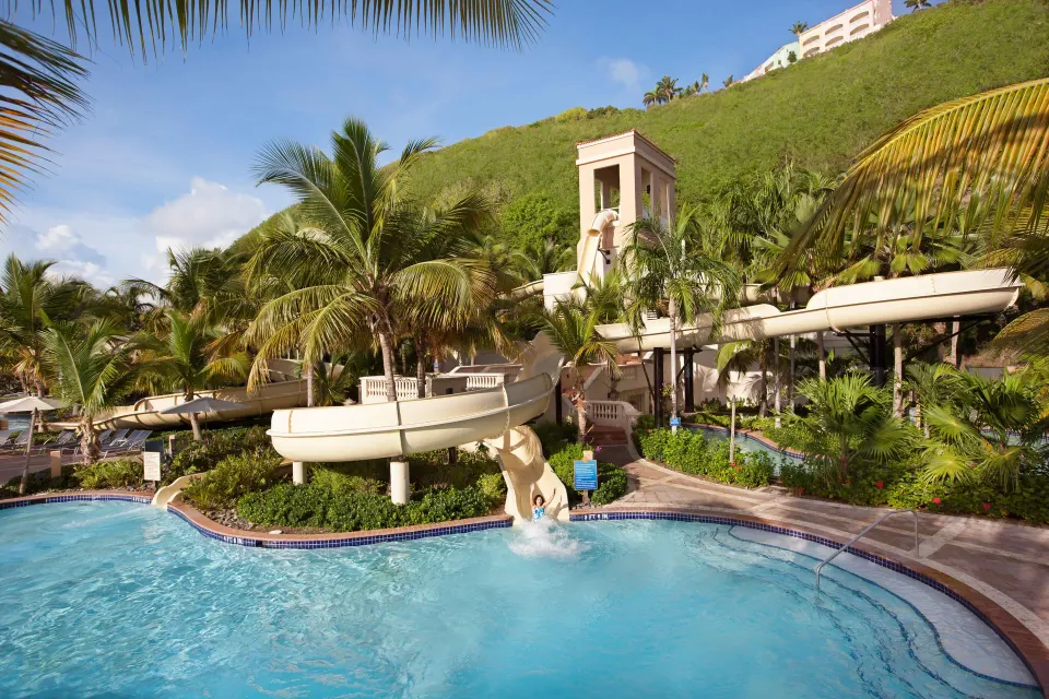Pool area with waterslide, palms, and hillside landscaping at El Conquistador Resort.