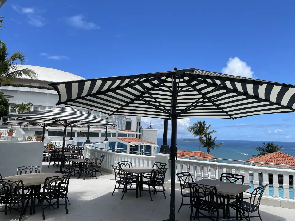 Outdoor terrace dining tables with striped umbrellas and ocean view at El Conquistador Resort.