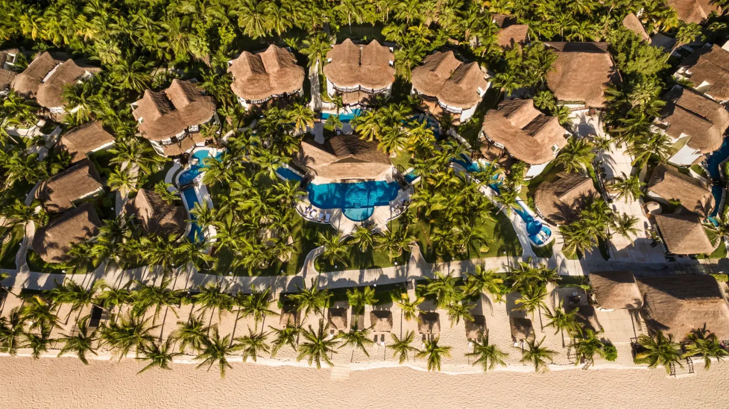 An aerial view shows casitas, pools, palms, and beach at El Dorado Casitas Royale.