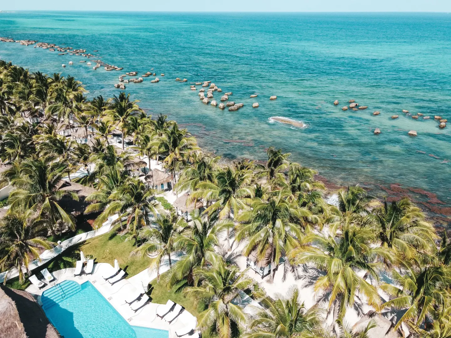 Aerial beachfront view with palms, loungers, pool, and turquoise sea at El Dorado Casitas Royale.