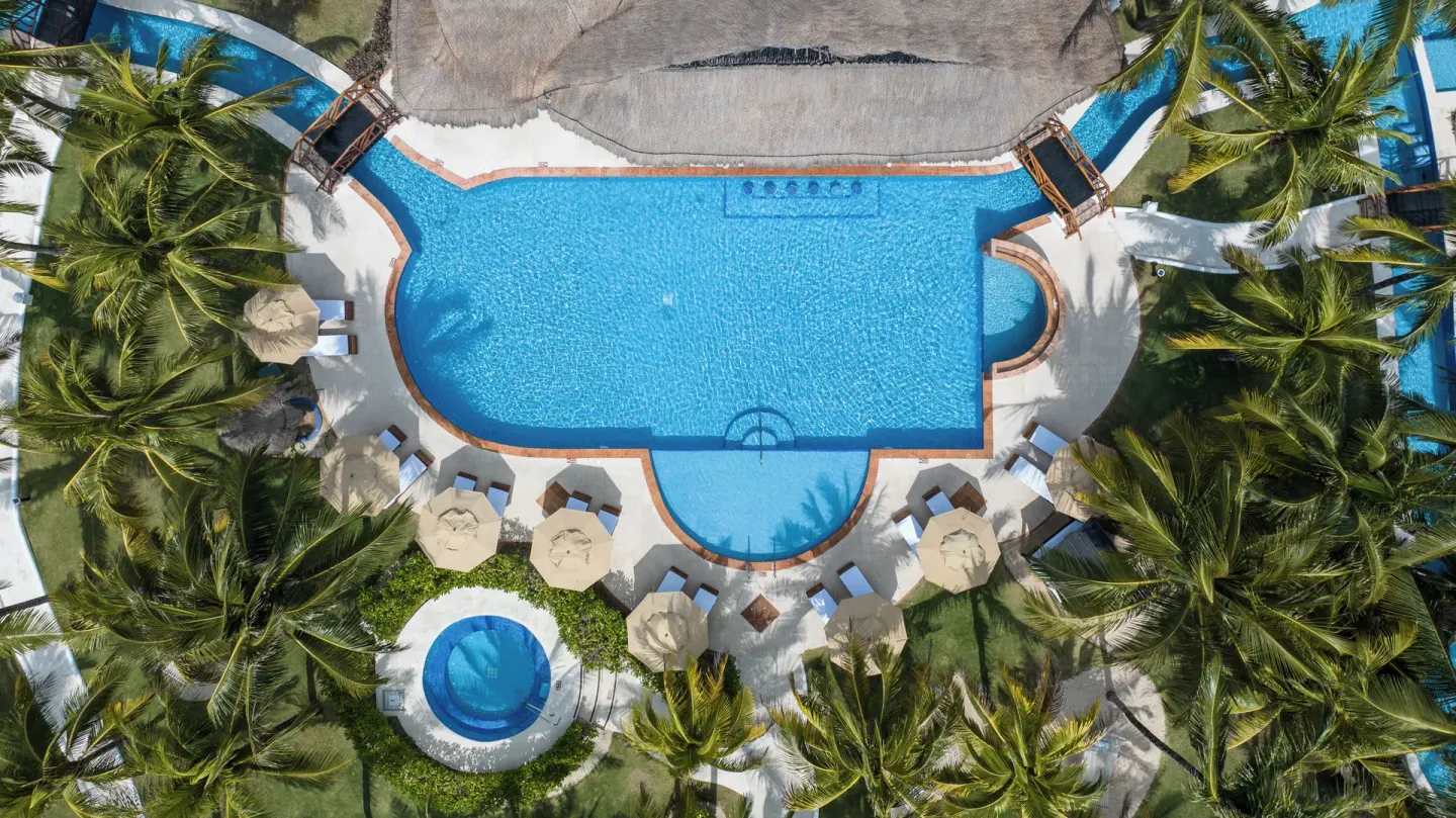 Overhead view of a large pool, loungers, umbrellas, and palms at El Dorado Casitas Royale.