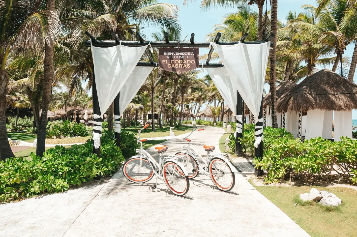 Palm-lined resort entrance with bicycles and welcome sign at El Dorado Casitas Royale.