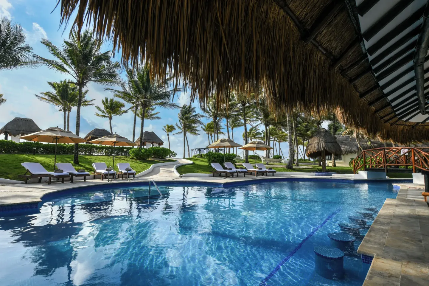 Resort pool with loungers, umbrellas, palms, and ocean beyond at El Dorado Casitas Royale.