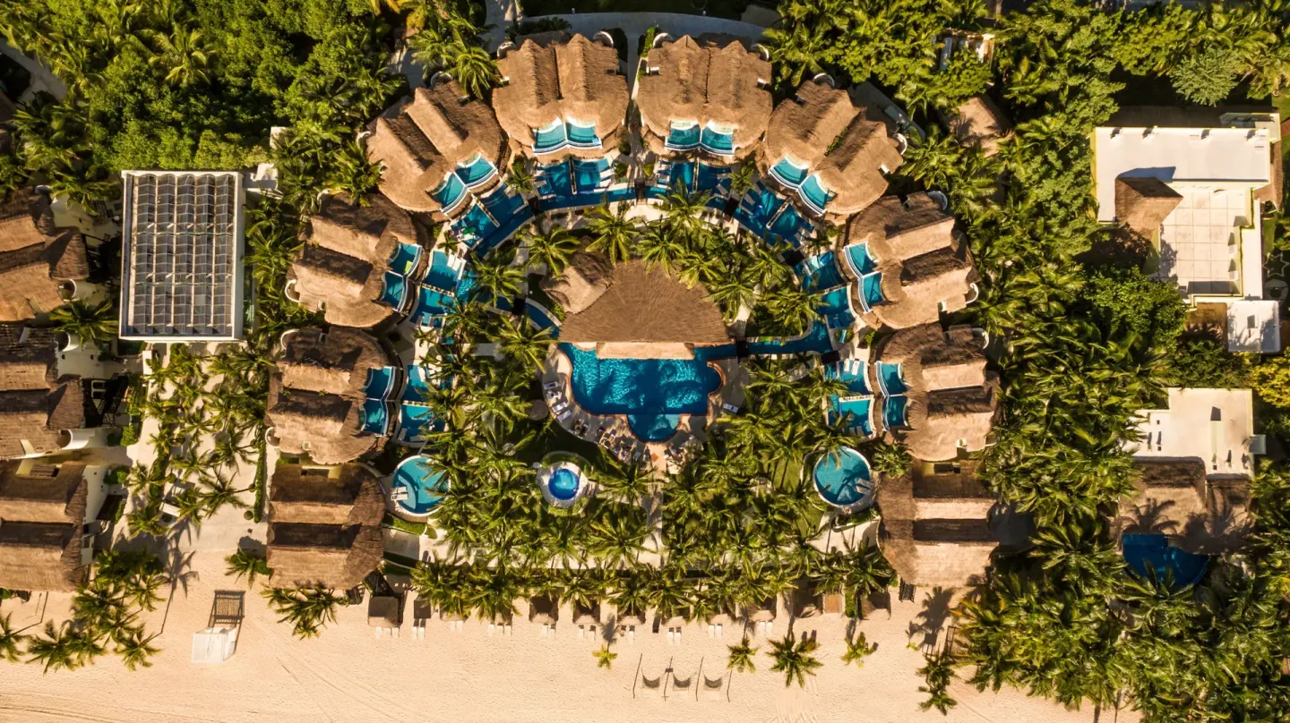 Top-down aerial view of semicircular casitas, pools, palms, and beach at El Dorado Casitas Royale.