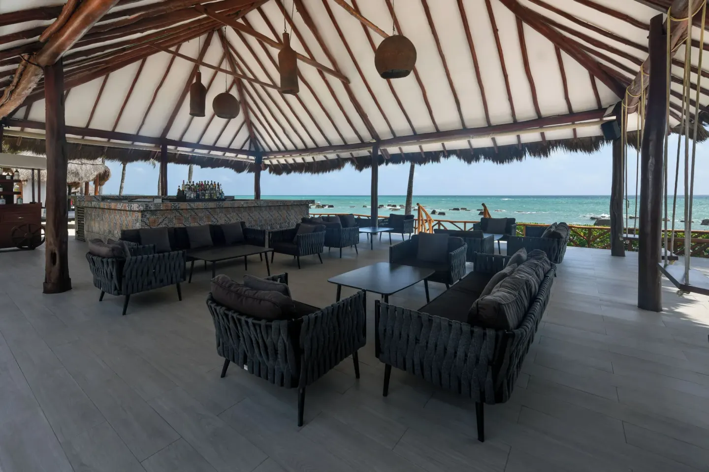 Covered seaside bar lounge with cushioned seating and ocean beyond at El Dorado Casitas Royale.
