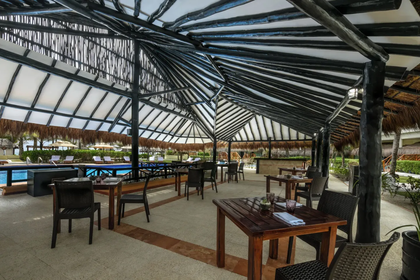 An open-air poolside restaurant with thatched roofing at El Dorado Casitas Royale.