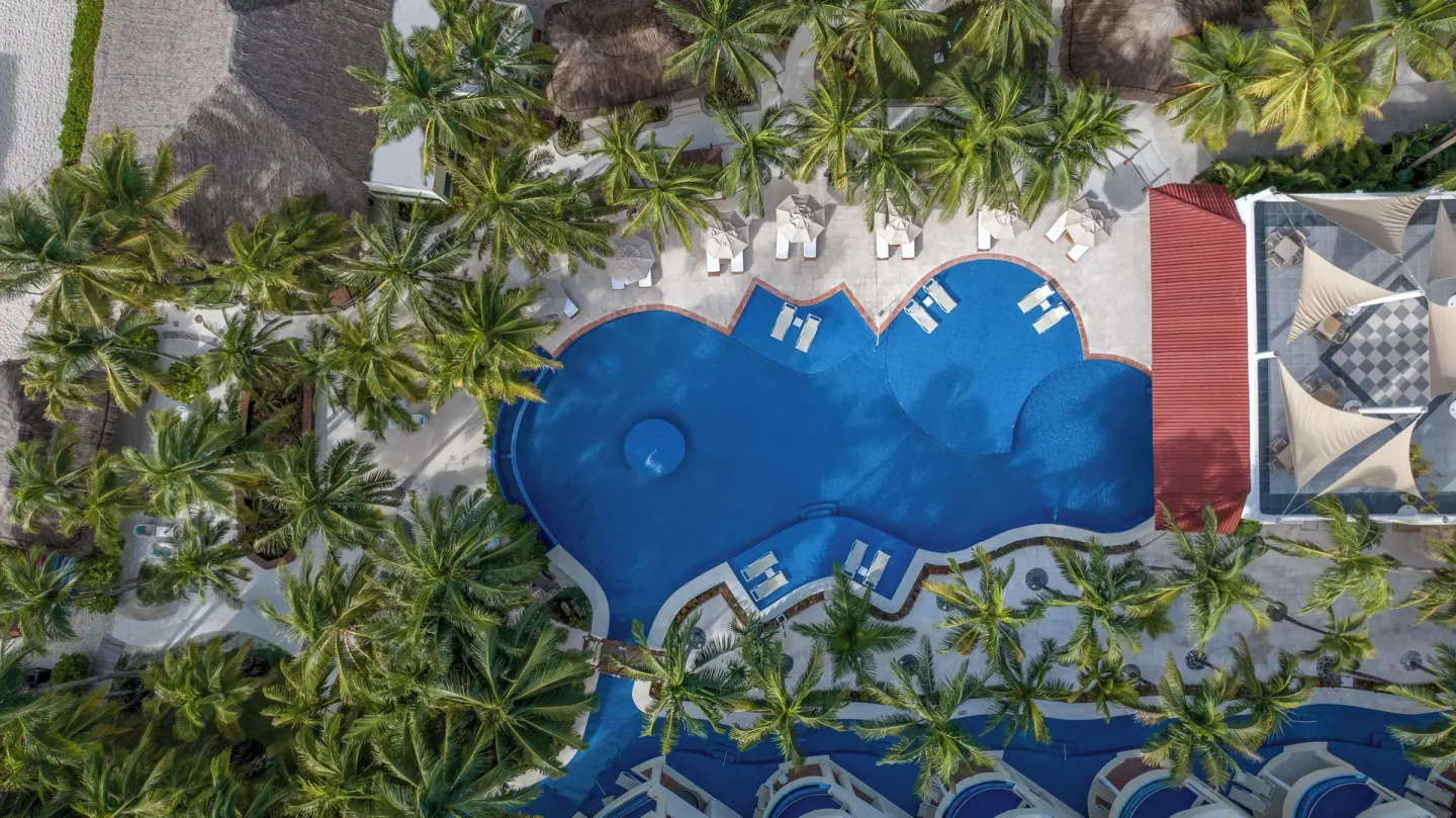 Aerial view of a curving resort pool at El Dorado Maroma Cenote, Underground Expedition.