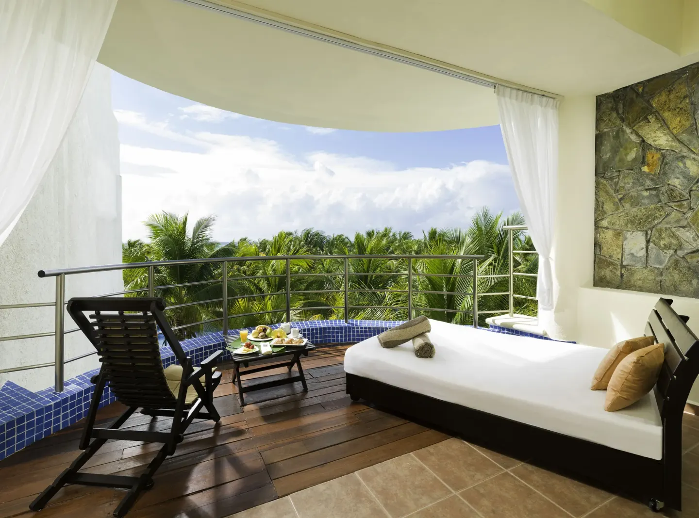 A balcony daybed overlooks palm trees at El Dorado Maroma Cenote, Underground Expedition.