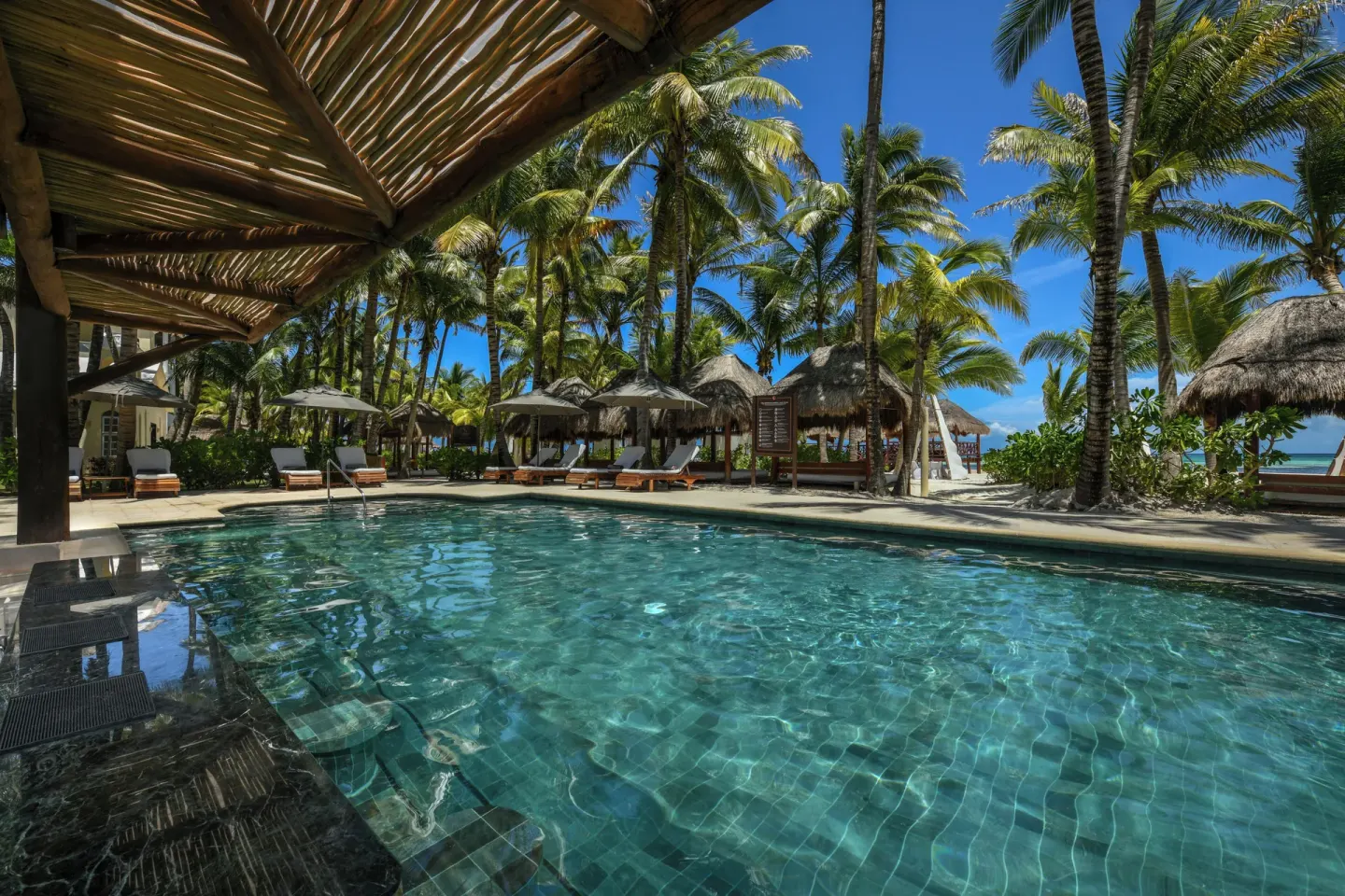 Beachside pool with palms and thatched shade at El Dorado Maroma Cenote, Underground Expedition.