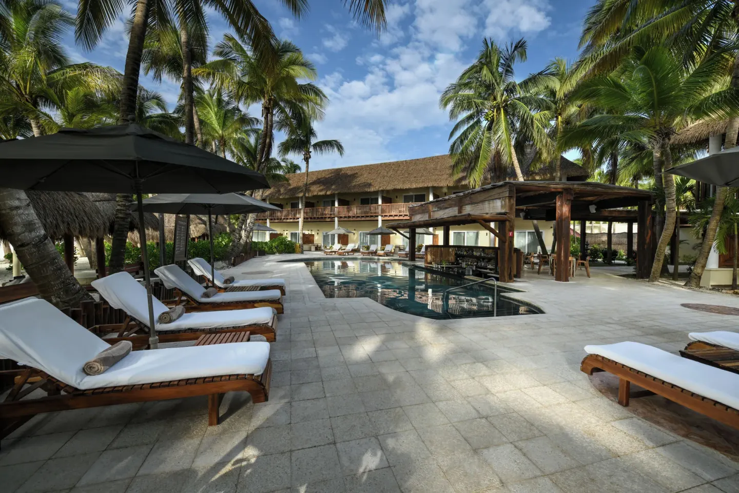 Palm-shaded pool deck with loungers at El Dorado Maroma Cenote, Underground Expedition.