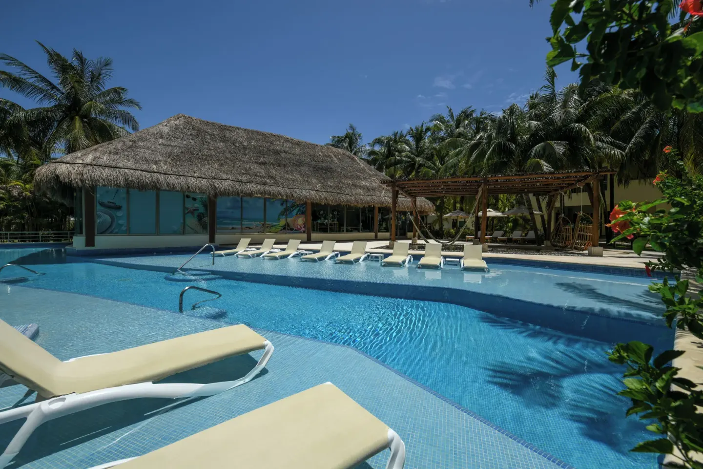 Pool with in-water loungers and palapa building at El Dorado Maroma Cenote, Underground Expedition.