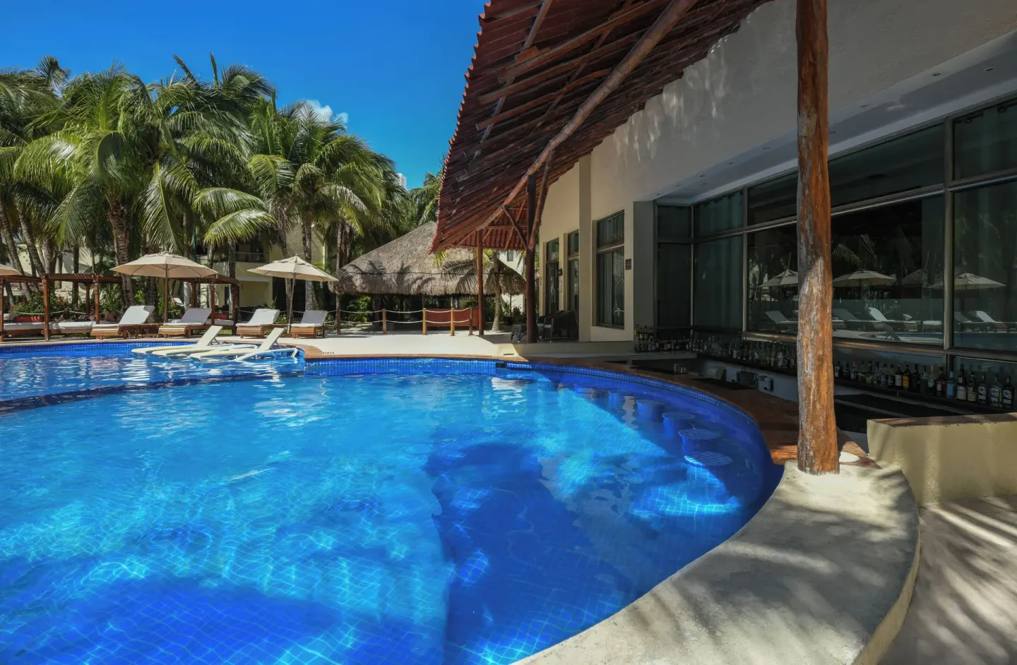 Pool with swim-up bar and palms at El Dorado Maroma Cenote, Underground Expedition.