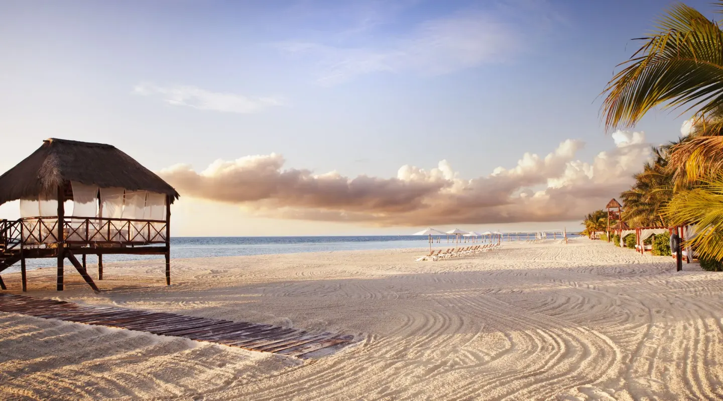 Sunlit beach with a thatched overwater hut at El Dorado Maroma Cenote, Underground Expedition.