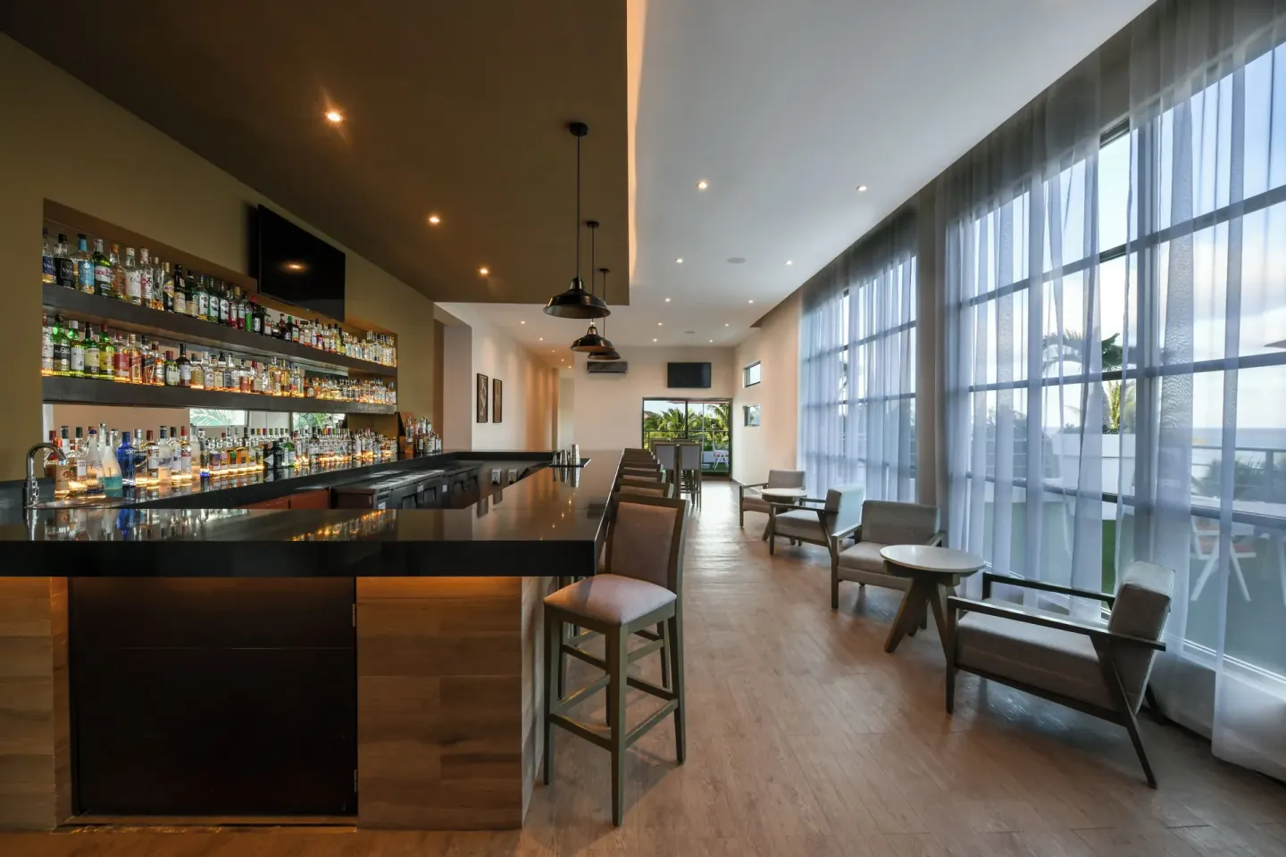 Modern bar with lounge seating and tall windows at El Dorado Maroma Cenote, Underground Expedition.