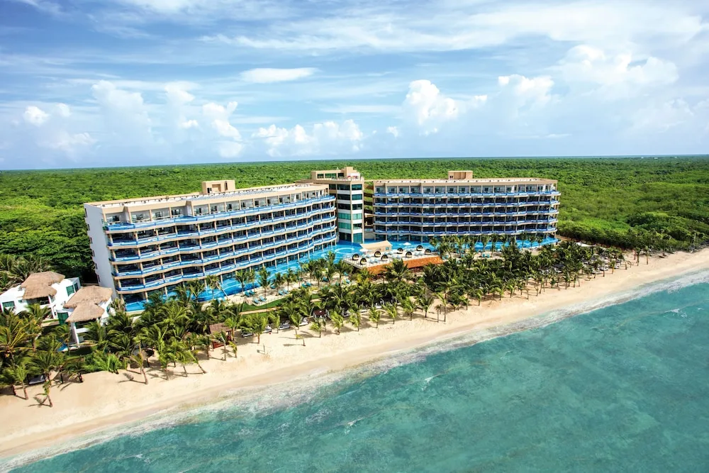 Wide aerial of the beachfront resort complex and palm-lined shore at El Dorado Seaside Suites