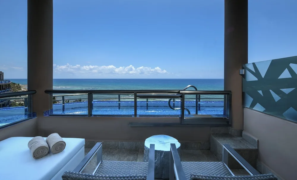 Ocean-view balcony with loungers and infinity pool beyond at El Dorado Seaside Suites