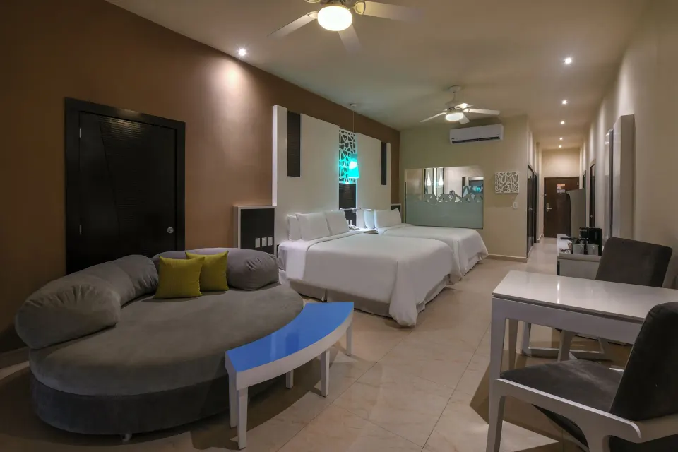 Junior suite at El Dorado Seaside Suites with two beds and lounge seating in warm lighting