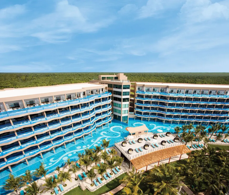 Resort buildings flanking a large pool with swim-up areas at El Dorado Seaside Suites