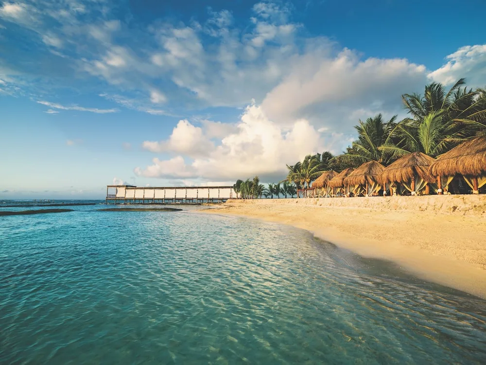 Sandy beach with palapas and a distant pier at El Dorado Seaside Suites