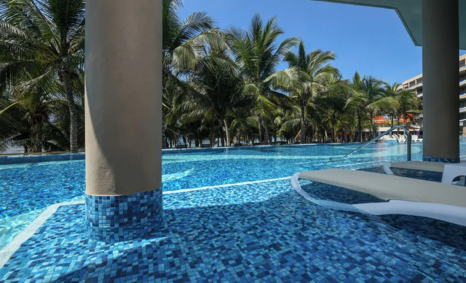 Swim-up pool area at El Dorado Seaside Suites with submerged loungers and palm trees