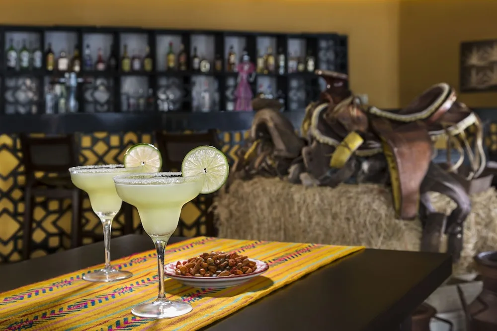 Two lime cocktails on a table with bar seating in the background at El Dorado Seaside Suites