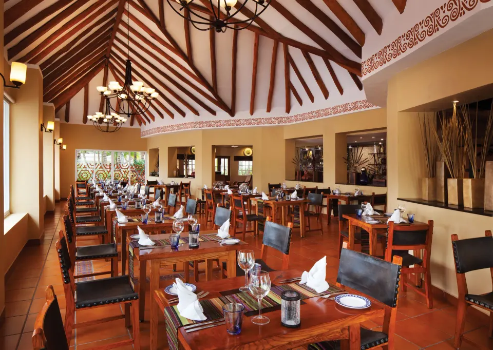 Large dining room with high beamed ceiling and set tables at El Dorado Seaside Suites