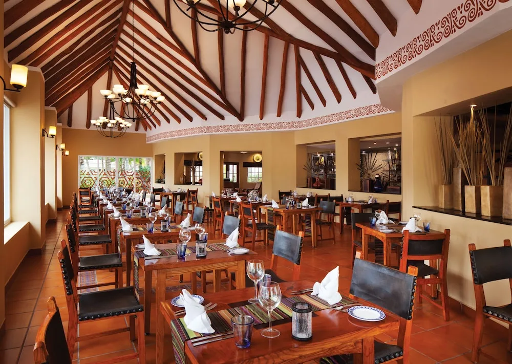 Spacious resort restaurant dining room with wooden tables and high beamed ceiling at El Dorado Seaside Suites