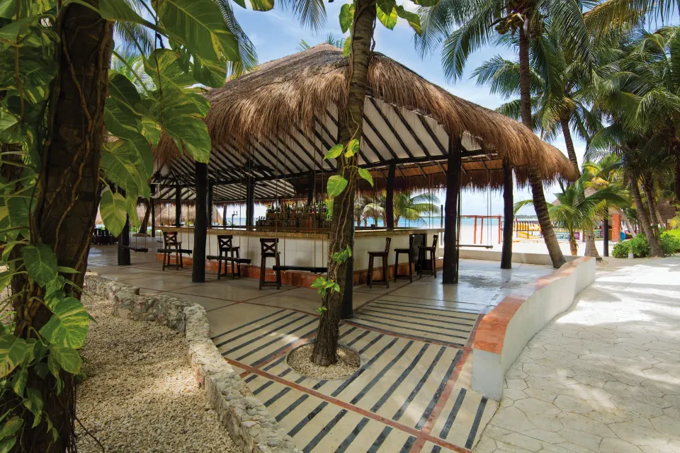 Open-air thatched bar with wooden columns overlooking the beach at El Dorado Seaside Suites
