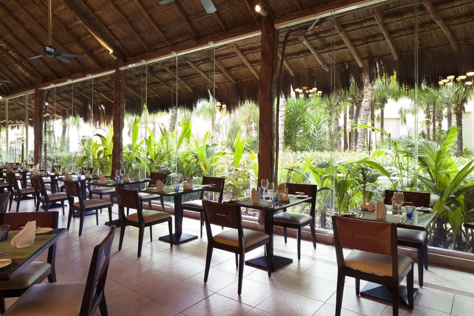Open-air thatched-roof restaurant with tables facing tropical landscaping at El Dorado Seaside Suites