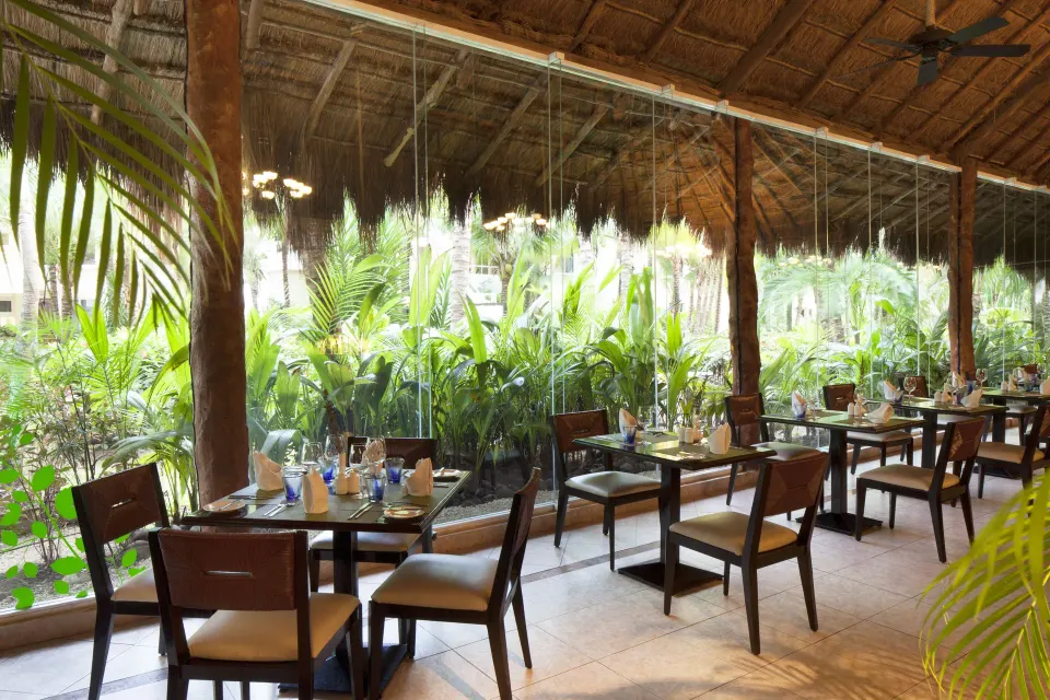 Open-air restaurant seating by tropical plants under a palapa at El Dorado Seaside Suites
