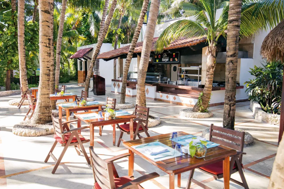Outdoor dining tables beneath palm trees near a poolside counter at El Dorado Seaside Suites