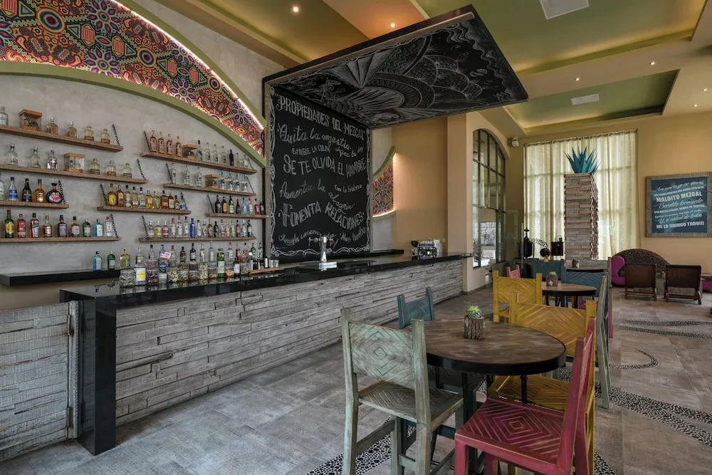 Long resort bar counter with colorful chairs and chalkboard menu at El Dorado Seaside Suites
