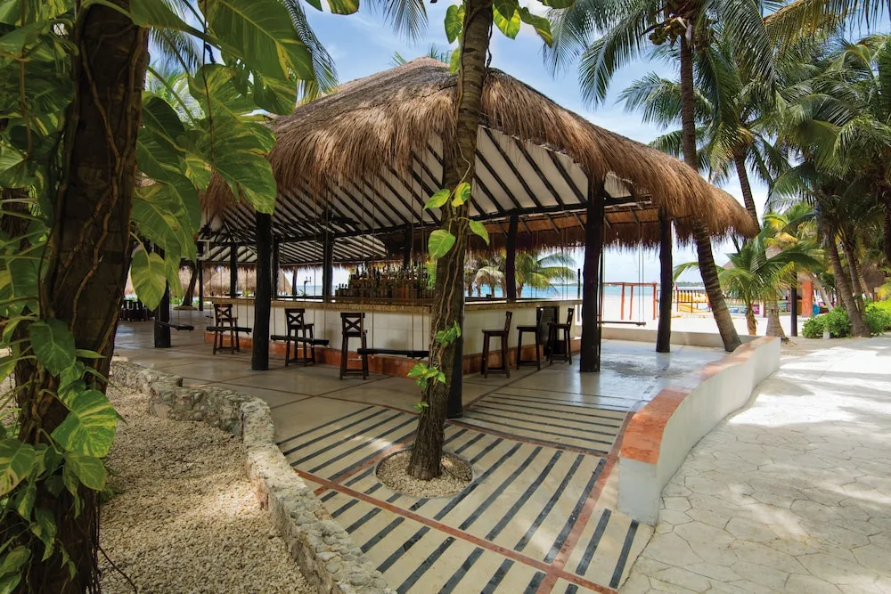 Thatched open-air beach bar under palm trees at El Dorado Seaside Suites