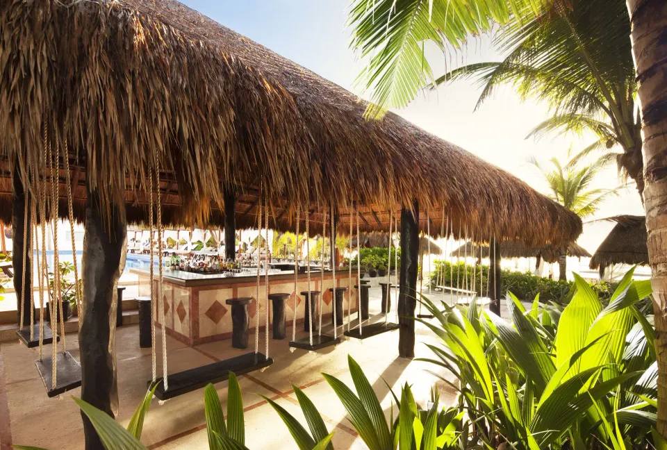 Thatched-roof outdoor bar with swing seats by the pool at El Dorado Seaside Suites