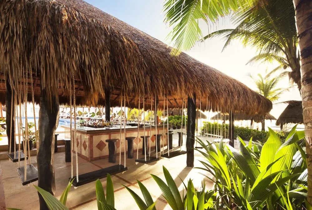 Thatched swim-up bar with swing seats and palapa roof at El Dorado Seaside Suites