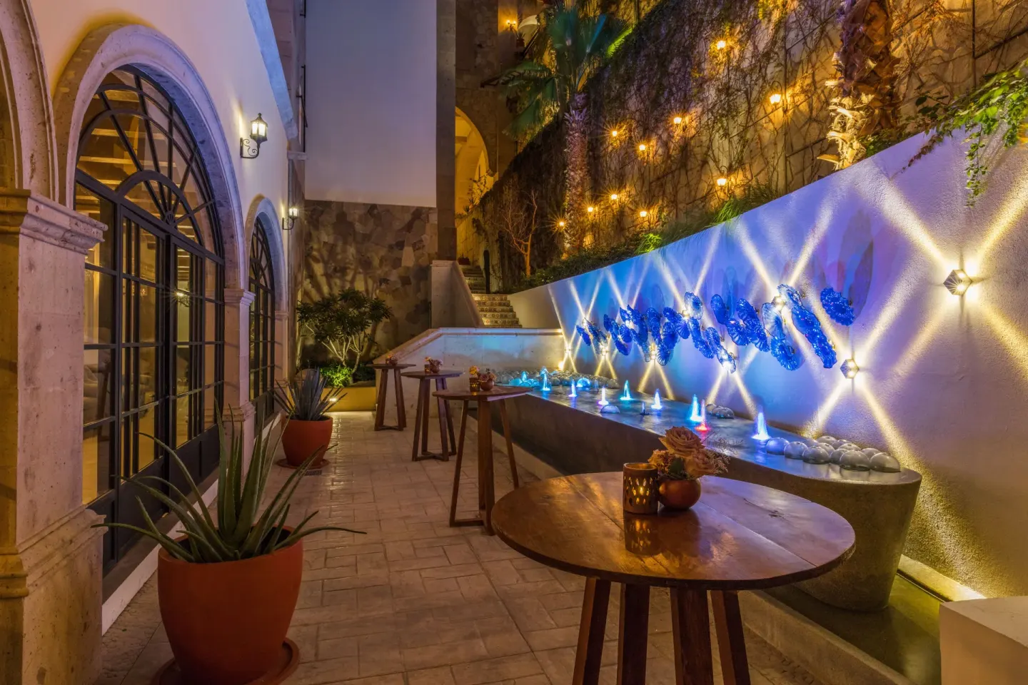 Evening terrace with arched windows, cocktail tables and a lit fountain at El Encanto at Hacienda Encantada.
