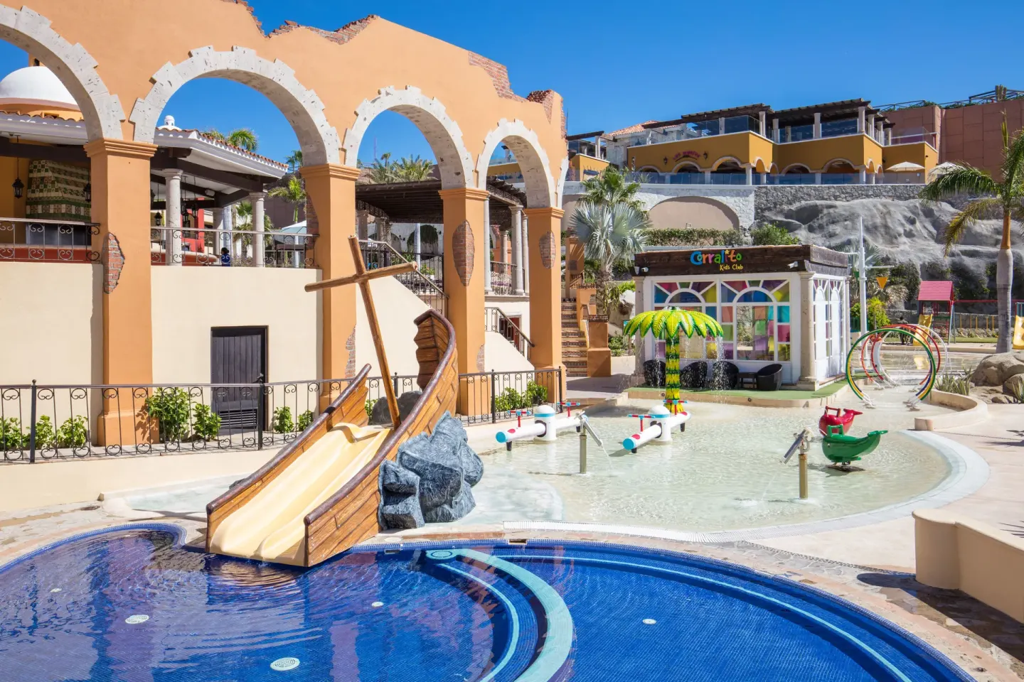 Kids pool with boat slide and arched resort buildings at El Encanto at Hacienda Encantada.