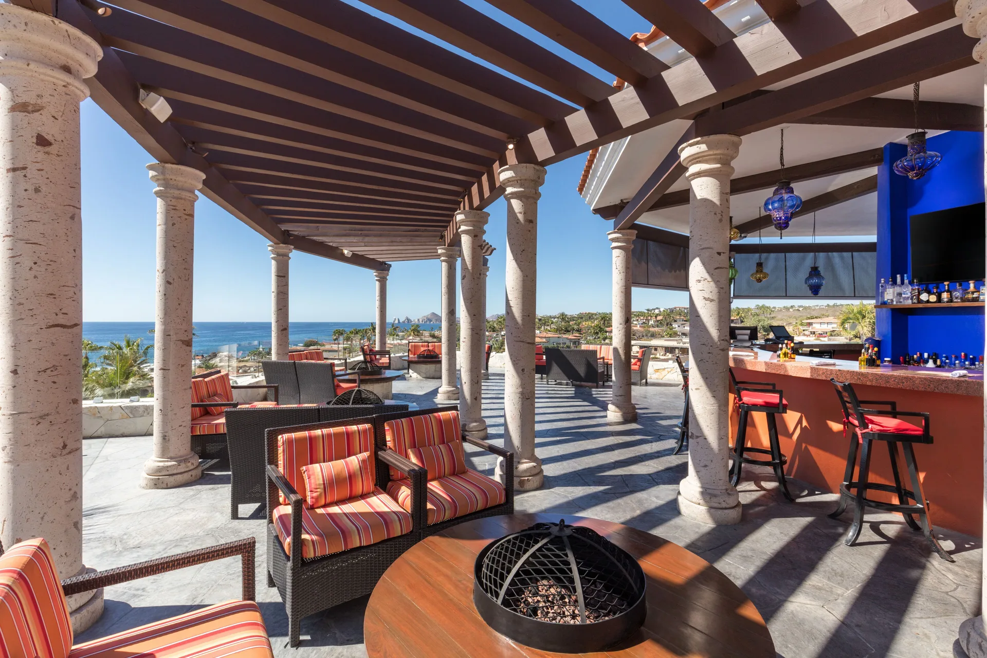 Open-air oceanview bar lounge at El Encanto at Hacienda Encantada with striped seating and columns.