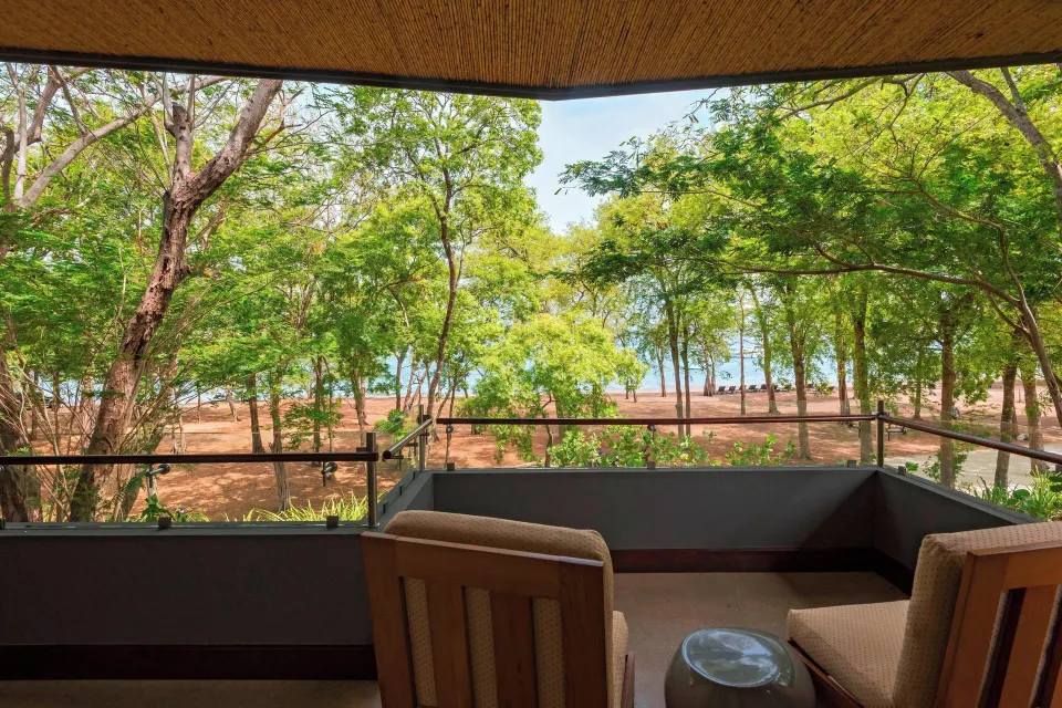 Balcony seating overlooking shaded trees and the beach at El Mangroove Papagayo