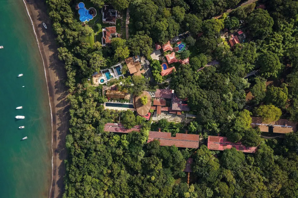 Top-down coastline aerial showing resort buildings and beach strip at El Mangroove Papagayo