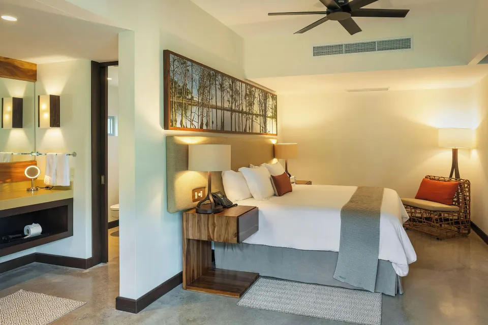 King bed with bedside lamps and rattan chair near bathroom at El Mangroove Papagayo