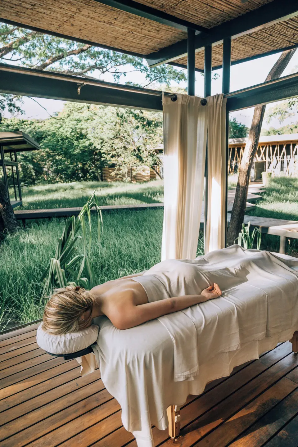 Guest on an outdoor massage table in a covered cabana overlooking the resort grounds at El Mangroove Papagayo