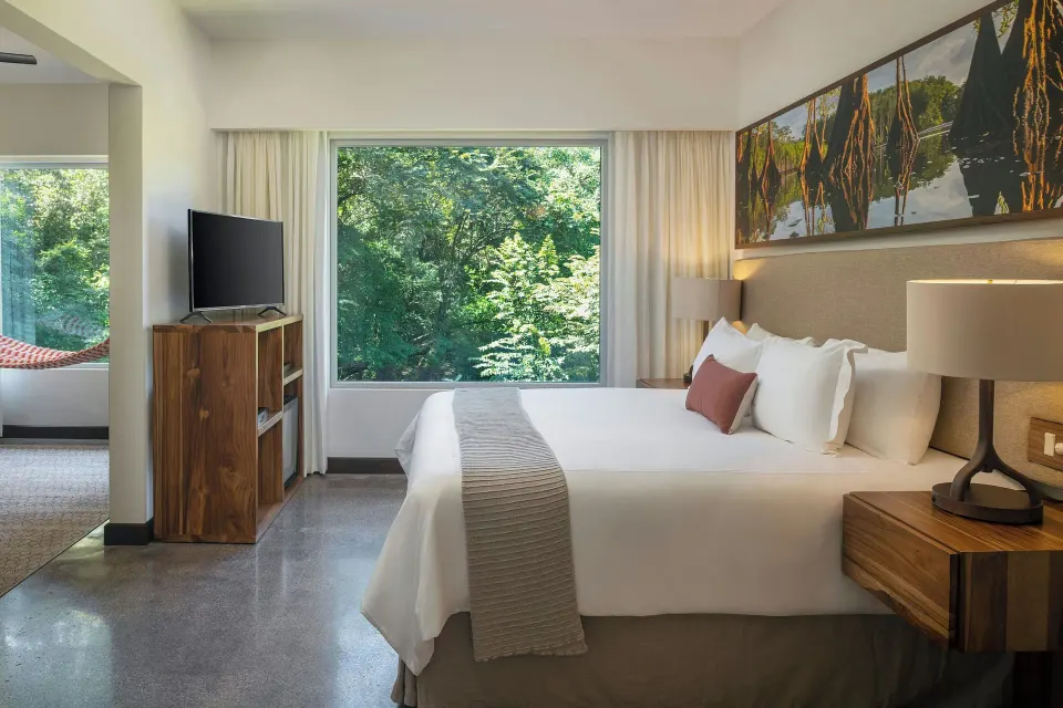 King bed with large window view of trees and separate seating area at El Mangroove Papagayo
