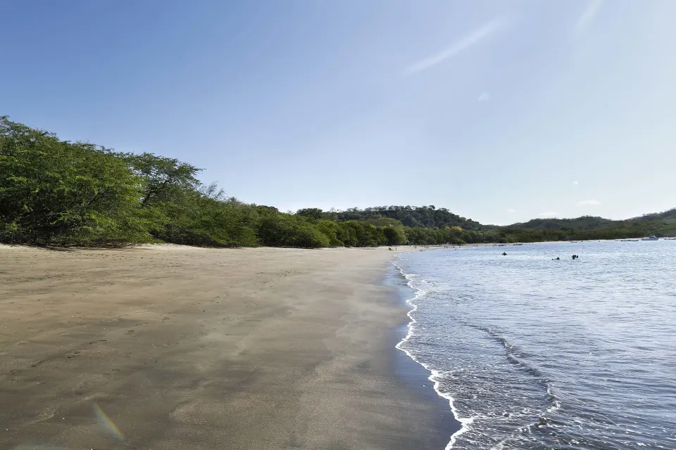 Long empty beach with ocean waves and distant swimmers at El Mangroove Papagayo